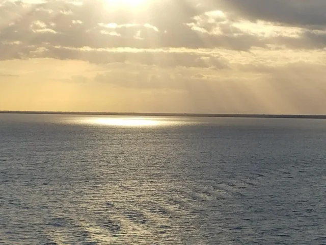 Raios de sol atravessam as nuvens e iluminam o mar até o horizonte.