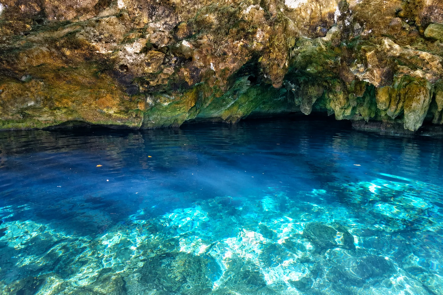 Cenote de águas azul-turquesa e transparentes sob uma abóbada de rocha, no México.