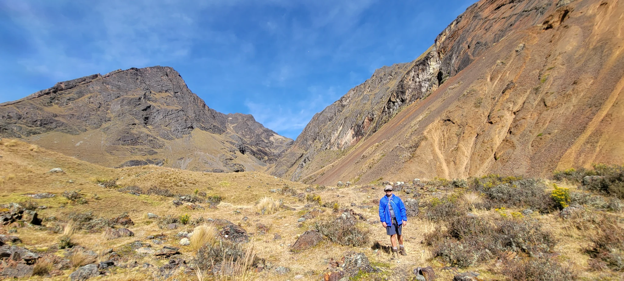 Uma pessoa caminha sozinha por um vale amplo entre montanhas áridas, nos Andes.