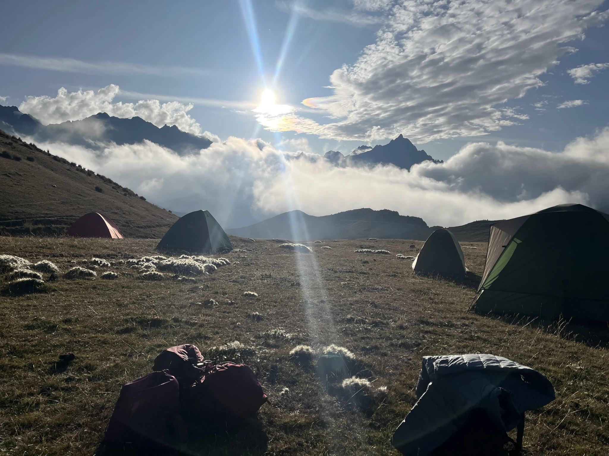 Acampamento no alto dos Andes: o sol atravessa as nuvens sobre as montanhas e as barracas no capim.
